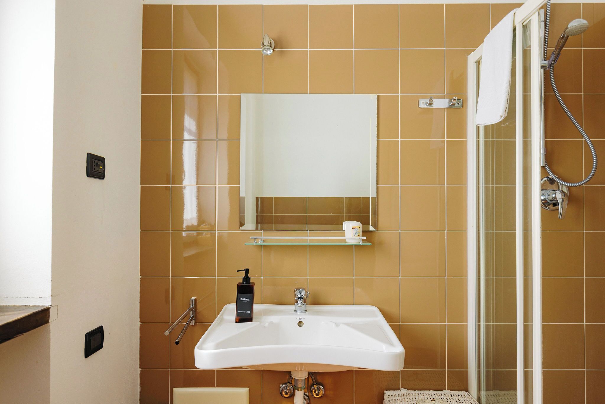 Un bagno con lavandino bianco, uno specchio, una doccia e un portasciugamani.