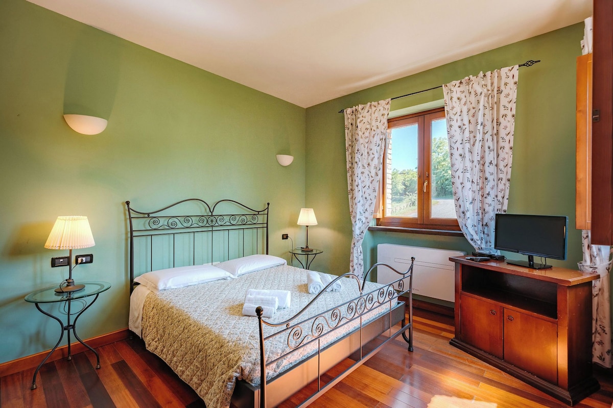 A bedroom with a bed, bedside lamps, a dresser, a television, and a window with curtains.