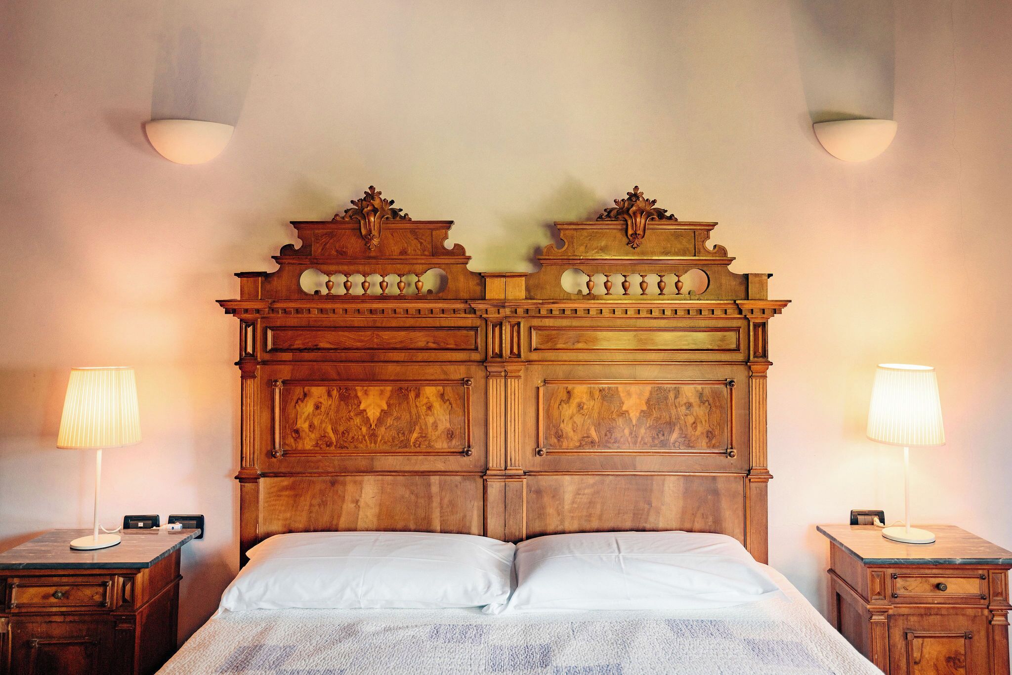 Un lit avec une tête de lit en bois, deux tables de chevet avec des lampes et une petite table de nuit avec une lampe.