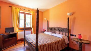 A bedroom with a four-poster bed, a wooden desk with a television, and a window with curtains.