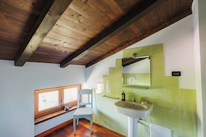 A bathroom with a wooden ceiling, a window with blinds, a sink with a mirror, and green tiles. - Tenuta Bellingeri - Locanda del Barco (SANT AGATA FOSSILI)