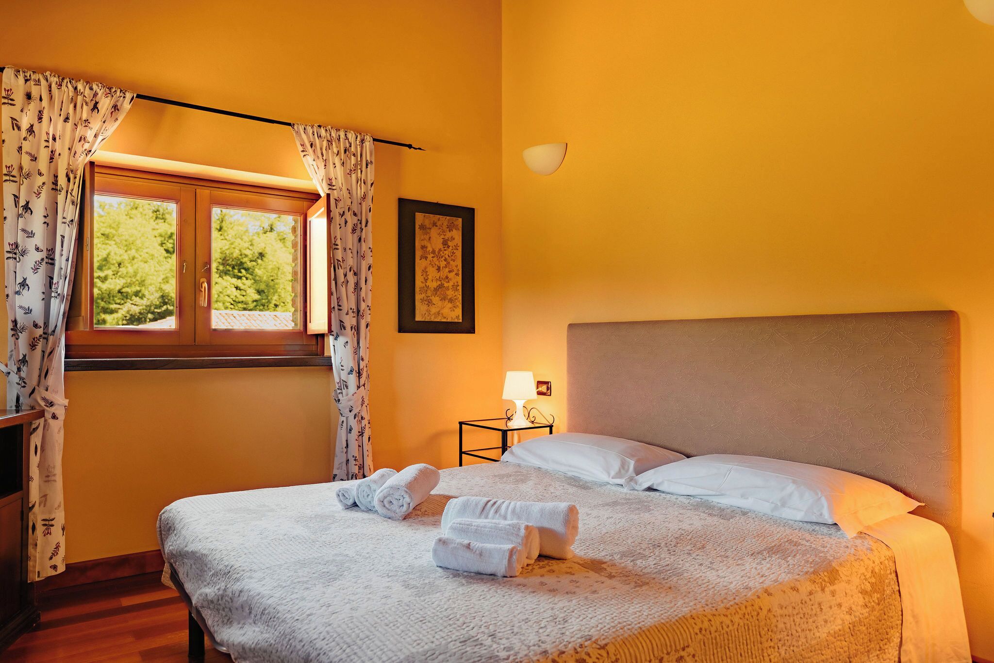Una habitación de hotel con cama, mesita de noche, lámpara y ventana con cortinas.