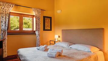 Una habitación de hotel con cama, mesita de noche, lámpara y ventana con cortinas.