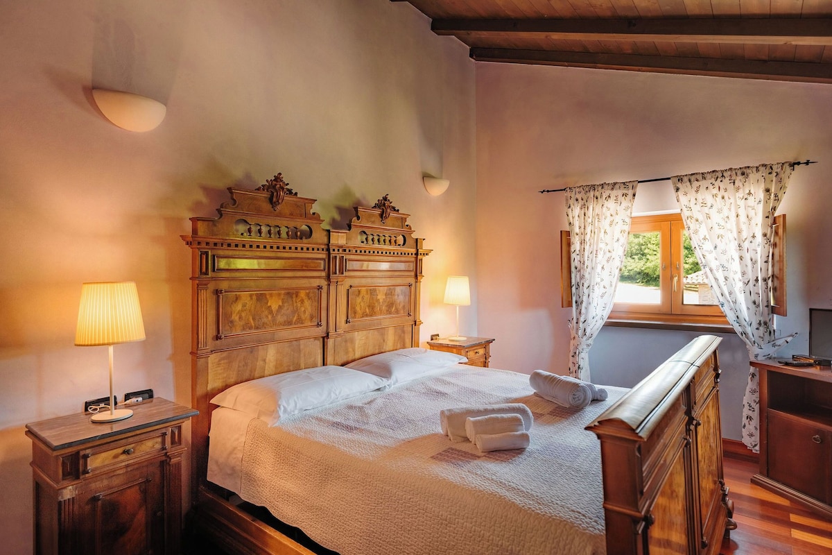 A bedroom with a wooden headboard, a bed with white linens, two bedside lamps, and a window with floral curtains.