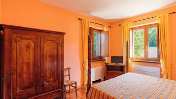 Una habitación con un armario de madera, una cama con ropa de cama a rayas, un escritorio con una computadora y una ventana con cortinas.