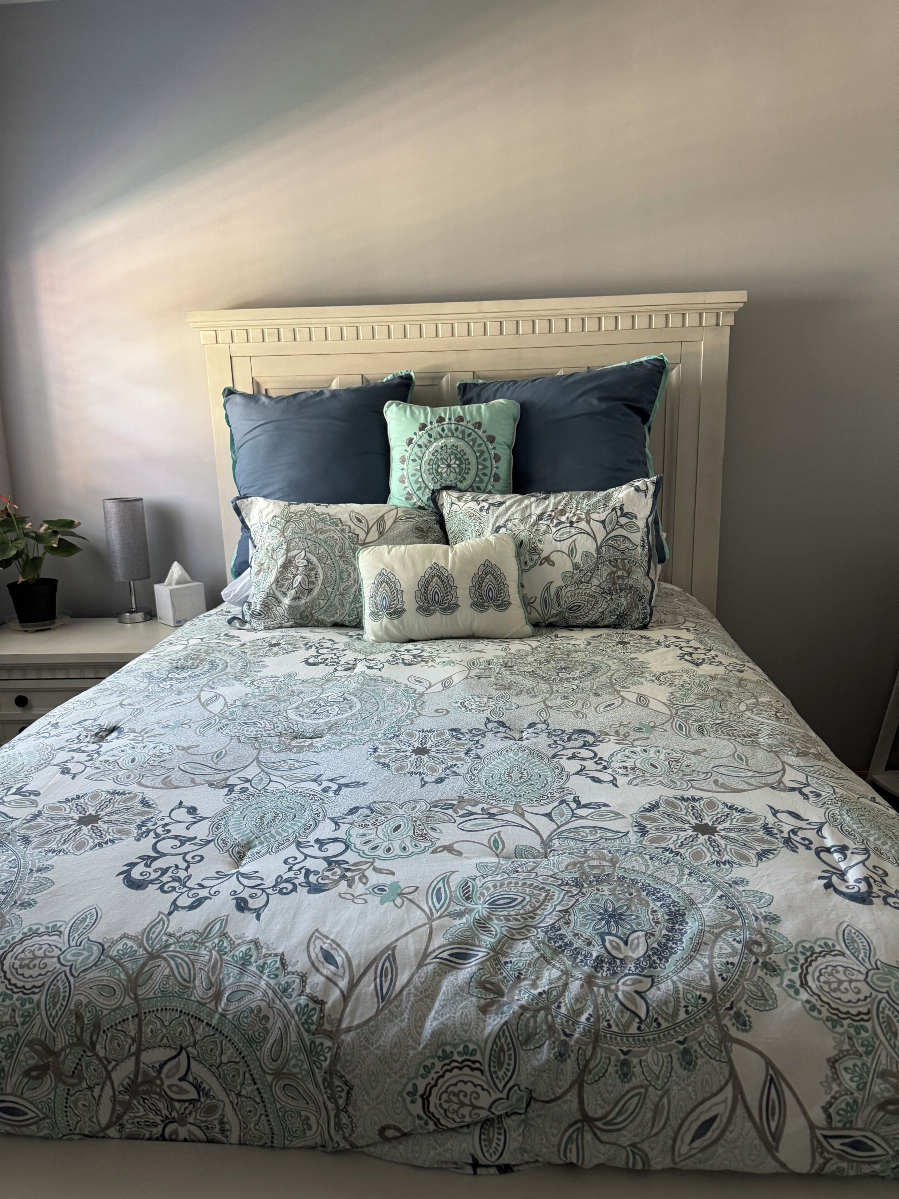A bed with a patterned bedspread, a headboard, and multiple pillows.