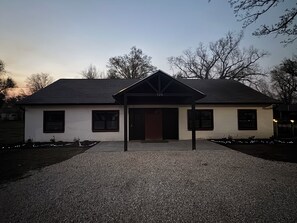 A single-story house with a dark roof, a front porch, and a driveway.