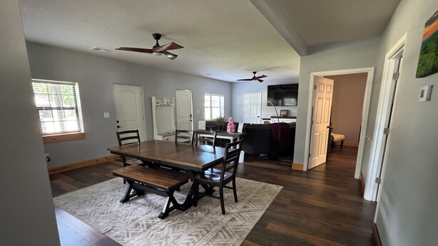 A dining area with a wooden table and chairs, a patterned rug, and a ceiling fan.