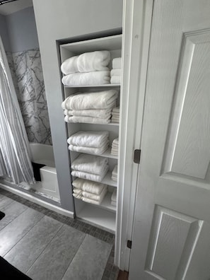 A bathroom with a marble wall, a white towel rack with neatly folded towels, and a closed door.