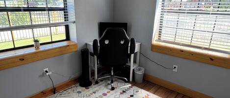 Een kamer met een kamerbreed tapijt, een zwarte bureaustoel en een raam met jaloezieën.