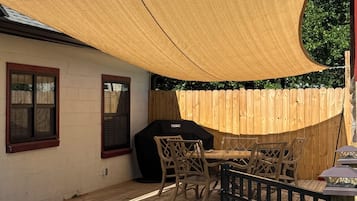 En baghave med træterrasse, grill og et bord med stole.