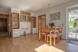 Zona pranzo con tavolo e sedie in legno, un armadietto bianco e un vaso con fiori.