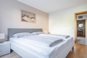 Una camera da letto moderna con un letto, comodini, un quadro appeso e un bagno visibile tramite una porta aperta.