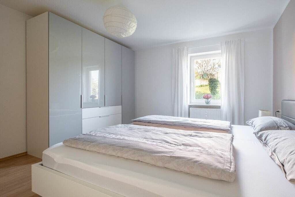 A bedroom with a large wardrobe, a bed with two pillows, and a window with curtains.