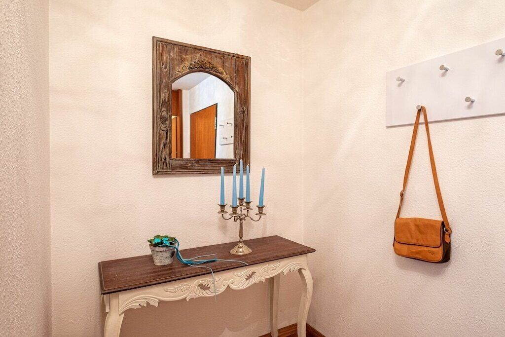 Une pièce avec une console blanche, un miroir, un chandelier avec des bougies, une petite plante et un sac brun accroché au mur.