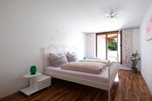 A bedroom with a bed, bedside table, and a window with a view of greenery. - Holiday apartment with 2 bedrooms (Meersburg)