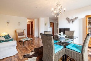 A living room with a glass-top dining table, wicker chairs, a white sofa, a cowhide rug, a chandelier, and a butterfly wall decoration. - Holiday apartment with 2 bedrooms (Meersburg)