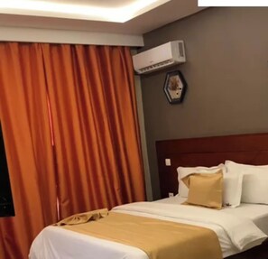 Habitación de hotel con cama, cortinas, equipo de aire acondicionado y un adorno en la pared.