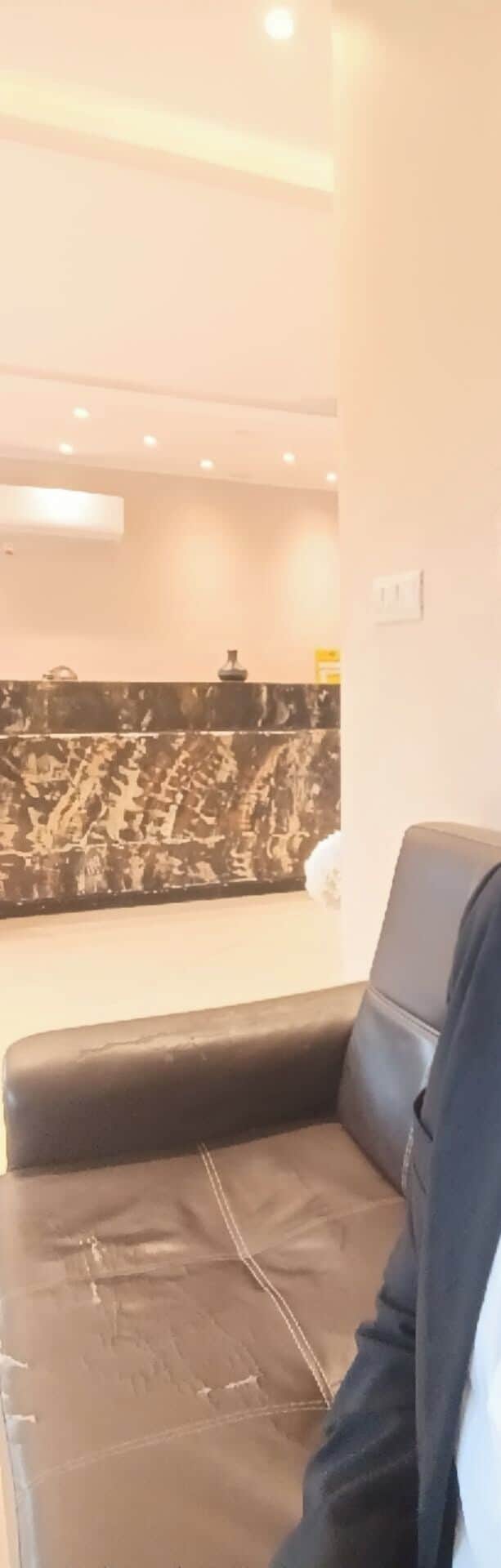 Un salón moderno con un sofá de cuero negro, una pared con estampado blanco y negro e iluminación empotrada en el techo.