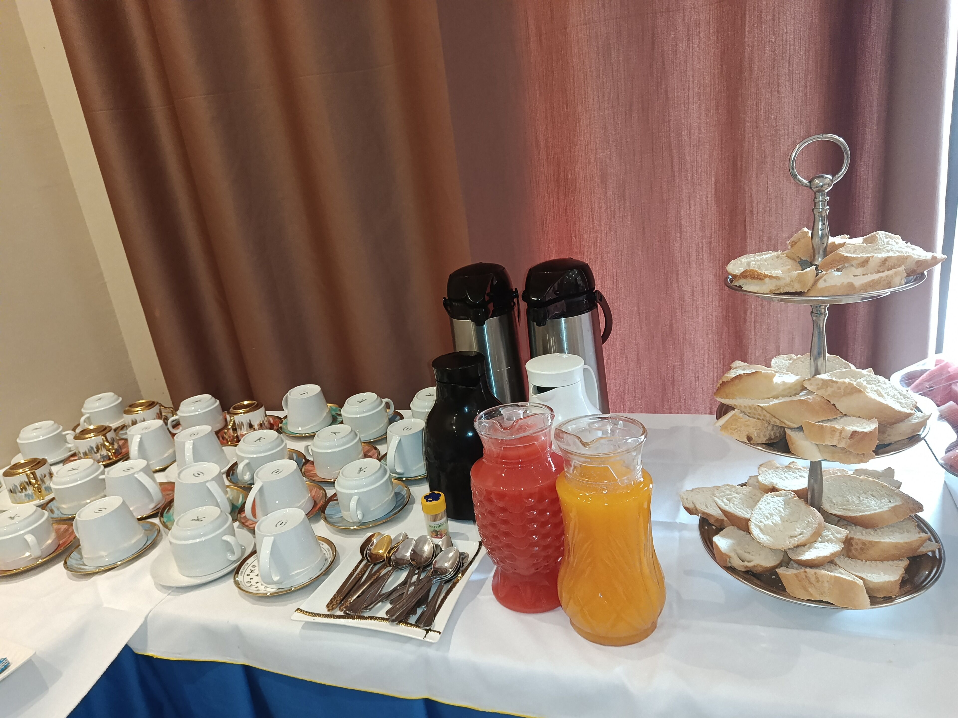Uma mesa com diversos itens de café da manhã, incluindo bules, xícaras, colheres e pão.