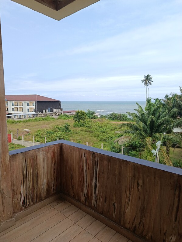 A balcony with a view of a building, a palm tree, and a body of water.
