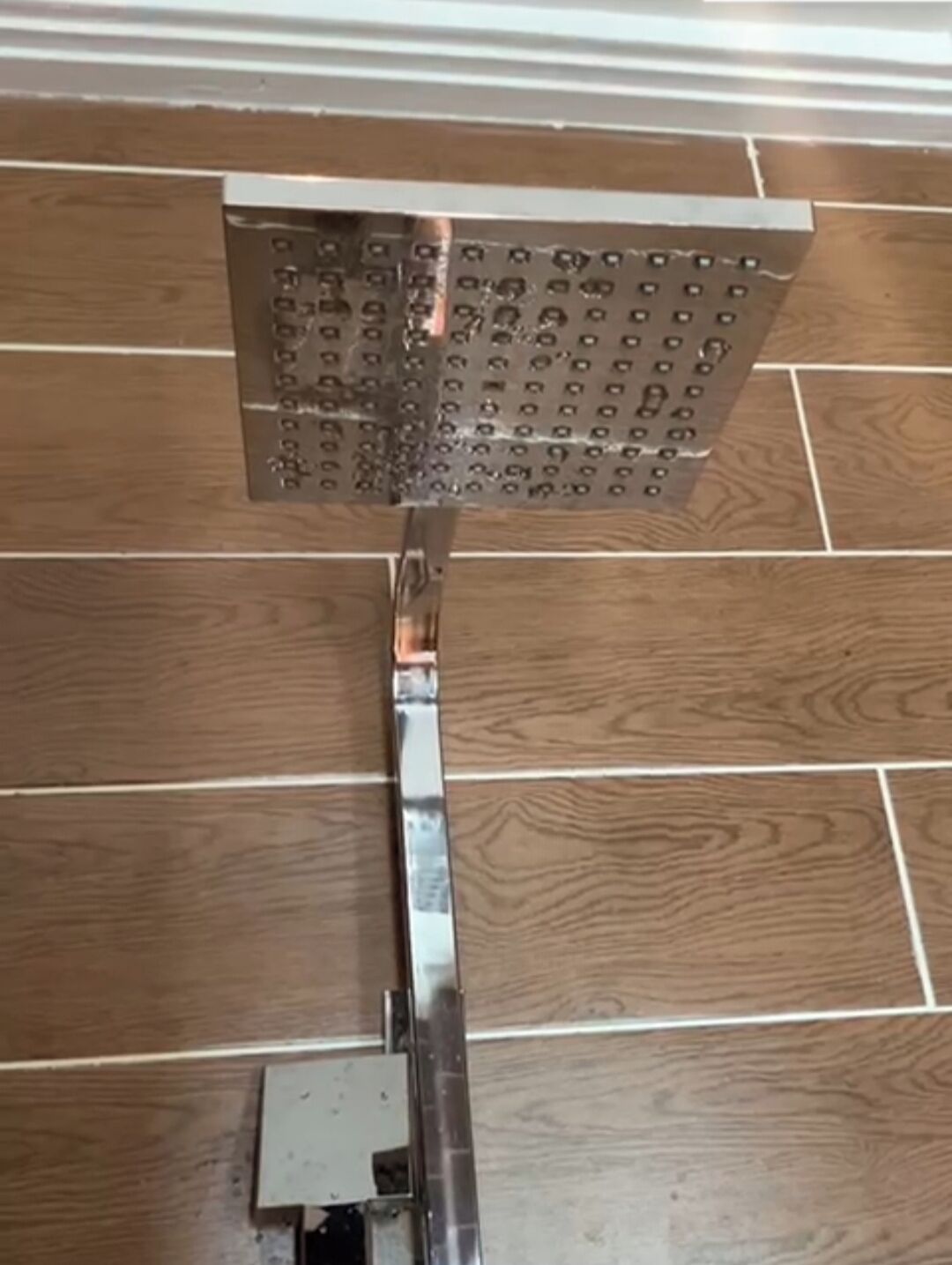 A showerhead mounted on a metal bracket attached to a wooden floor.