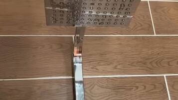 A showerhead mounted on a metal bracket attached to a wooden floor.