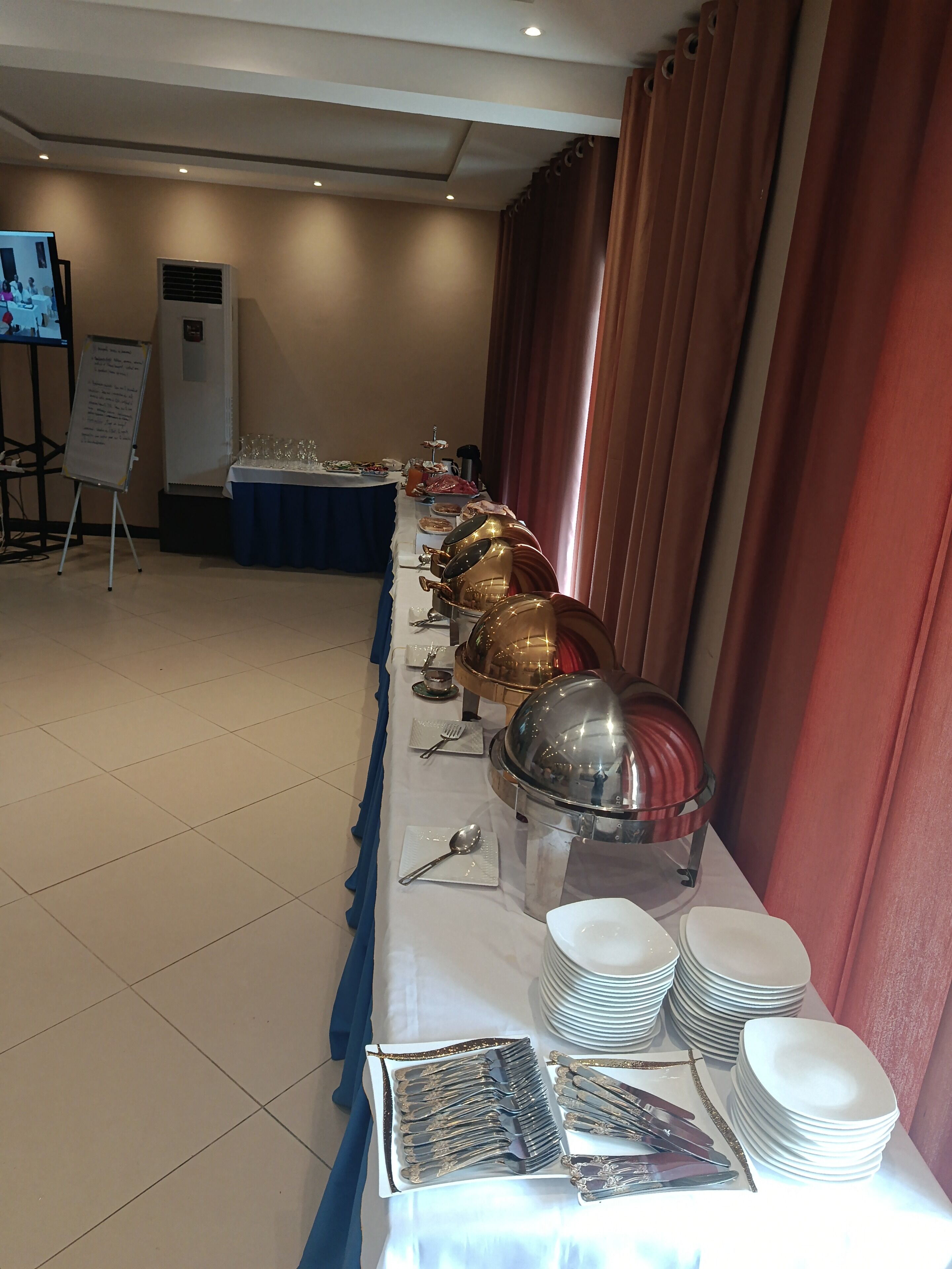 Disposição de buffet com mesa grande, pratos, talheres e apresentação de comida.