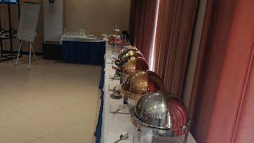 Disposição de buffet com mesa grande, pratos, talheres e apresentação de comida.