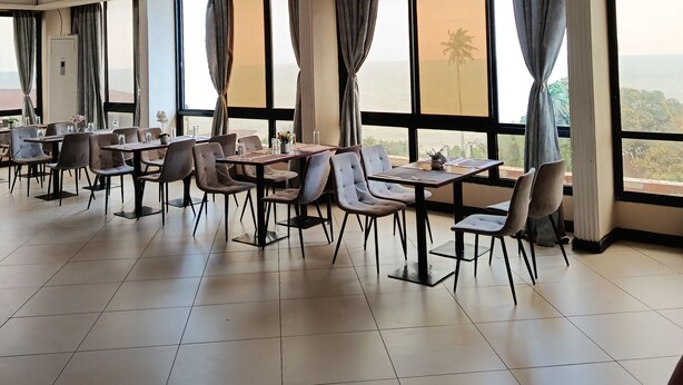 Un vaste espace dédié à la salle à manger, avec de nombreuses tables et chaises, de grandes fenêtres dotées de rideaux et une vue sur la mer.