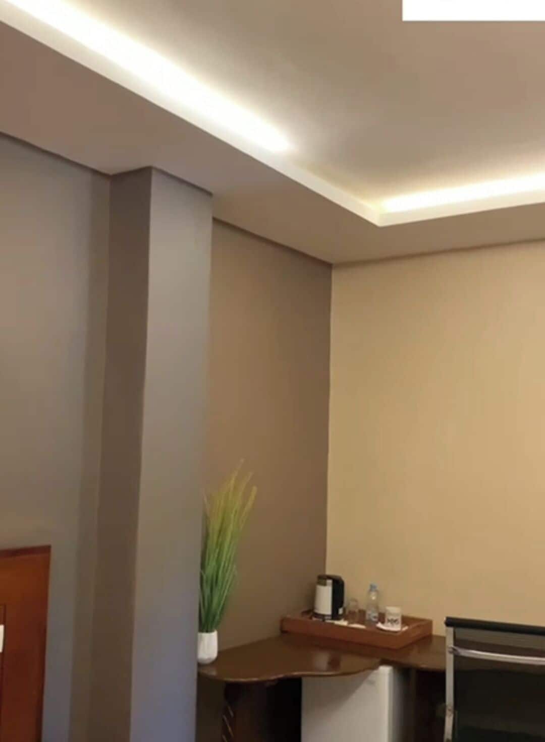 Quarto de hotel com escrivaninha de madeira, uma pequena planta em vaso, cafeteira e bandeja com xícara e copo.