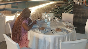 Une table à manger dressée pour deux personnes, avec des bouteilles d’eau et des verres, entourée de chaises blanches.