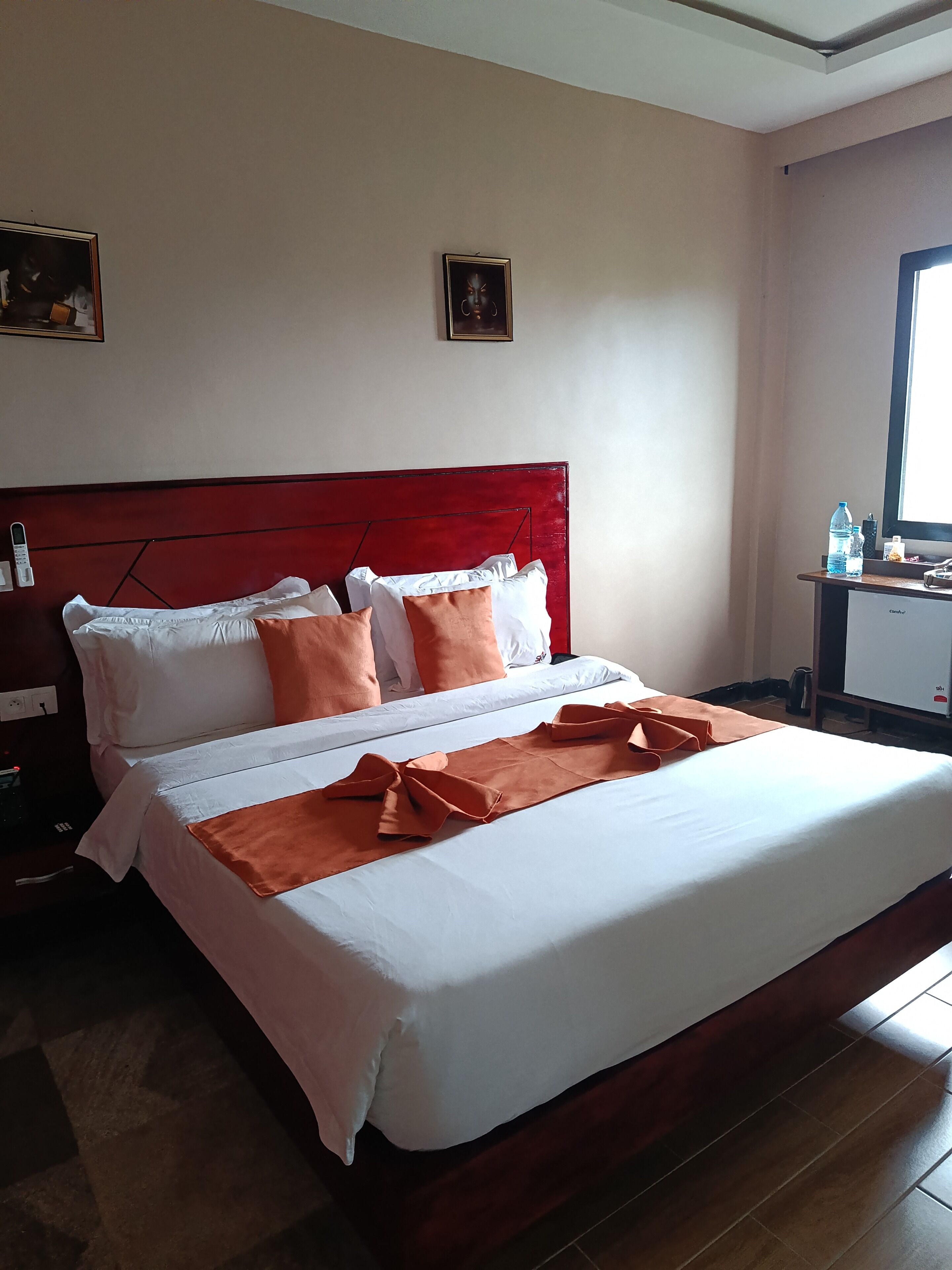 Een hotelkamer met een bed, kussens, een nachtkastje, een bureau met een computer en een raam.