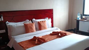 Een hotelkamer met een bed, kussens, een nachtkastje, een bureau met een computer en een raam.