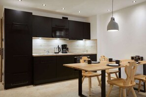 A modern kitchen with dark cabinetry, a wooden dining table, and a pendant light. - Riffelriss in the Chalet Zugspitzerei (Grainau)