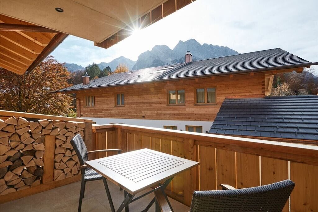Un balcon en bois, agrémenté d’une table et de chaises, qui offre une vue sur un paysage montagneux.