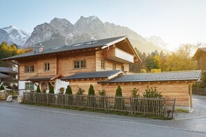 Une maison en bois à deux étages, dotée d’un balcon, qui se dresse sur un fond de paysage montagneux.