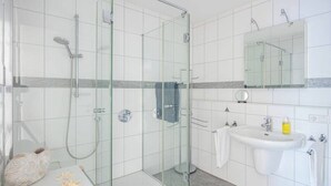 Un baño moderno con ducha de vidrio, lavamanos con espejo y un perchero para toallas.