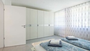 Un dormitorio con cama, armario y ventana con cortinas.