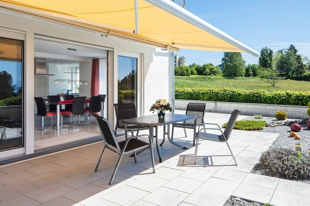 Eine Außenpatio mit Tisch und Stühlen, einem gelben Sonnensegel und Blick auf eine grüne Landschaft.