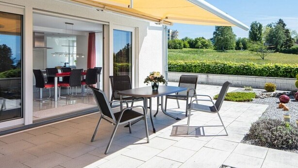 Un patio al aire libre con una mesa y sillas, un toldo amarillo y vista a un paisaje verde.