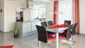 Una cocina moderna con comedor, que incluye una mesa de vidrio, sillas negras y un cojín rojo.