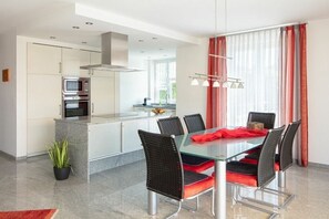 Eine moderne Küche mit Essbereich, ausgestattet mit einem Glastisch, schwarzen Stühlen und einem roten Kissen.