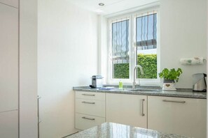 Une cuisine moderne avec une fenêtre, des armoires blanches et un plan de travail en granit.