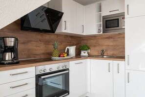 Una cocina moderna con armarios blancos, horno empotrado, microondas y cafetera.