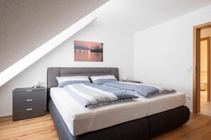 Un dormitorio con cama, mesita de noche, un cuadro en la pared y una puerta de madera.