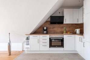 Una cocina moderna con armarios blancos, encimera de madera y horno empotrado.