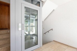 A modern interior with a glass door leading to a balcony, a wooden staircase, and a white textured wall. - Holiday apartment with 1 bedroom (Überlingen)