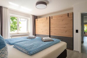 A bedroom with two beds, a window with curtains, a wooden headboard, and a ceiling light fixture. - Holiday apartment with 1 bedroom (Überlingen)