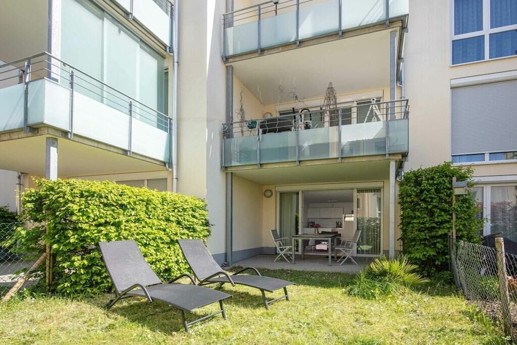 Un edificio residencial de dos plantas con balcón, zona de estar al aire libre y un jardín cuidado.